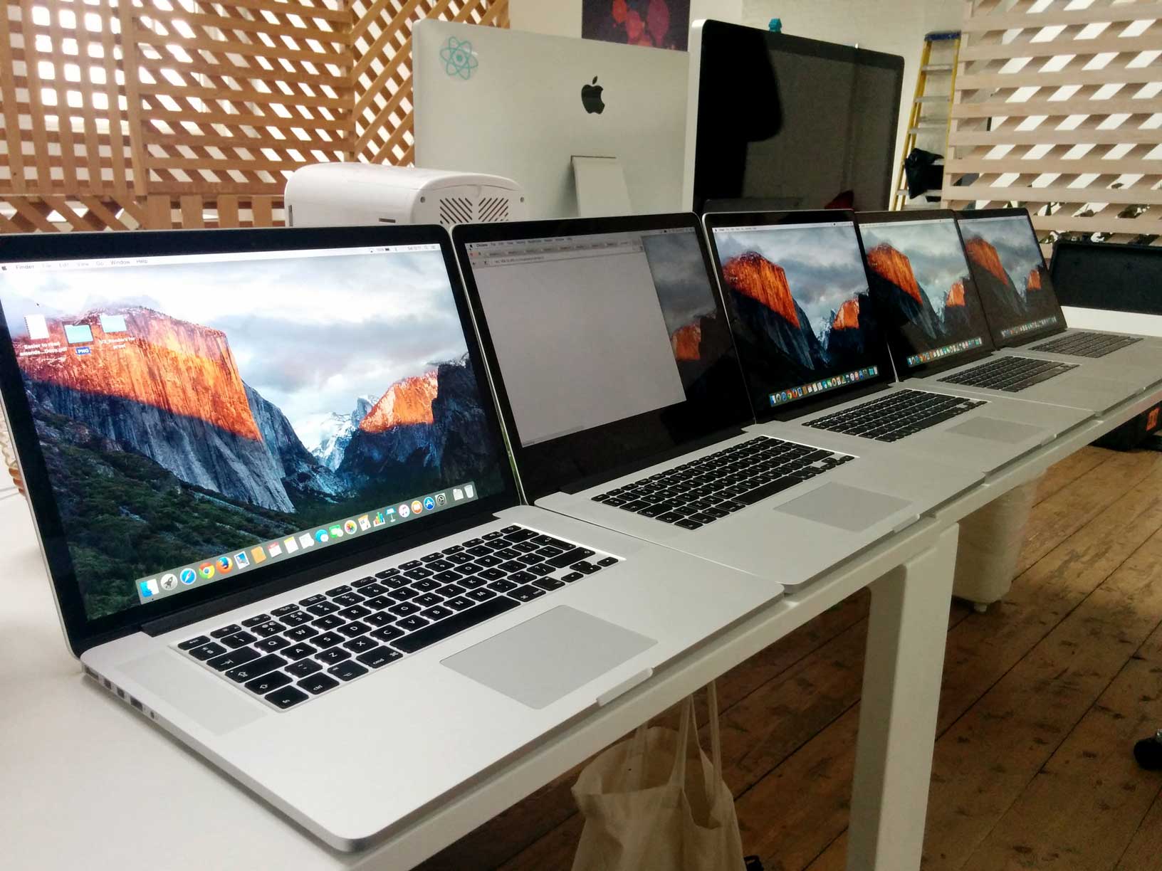 Five identical MacBook Pros lined up in a row on a desk